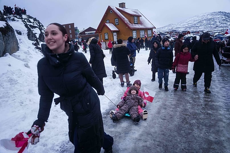 Grönland'ın Nuuk kentindeki ABD konsolosluğu önünde Trump'ın Grönland'a yönelik politikasını protesto eden bir kadın çocuklarını kucaklayarak çekiyor, 17 Ocak 2026.
